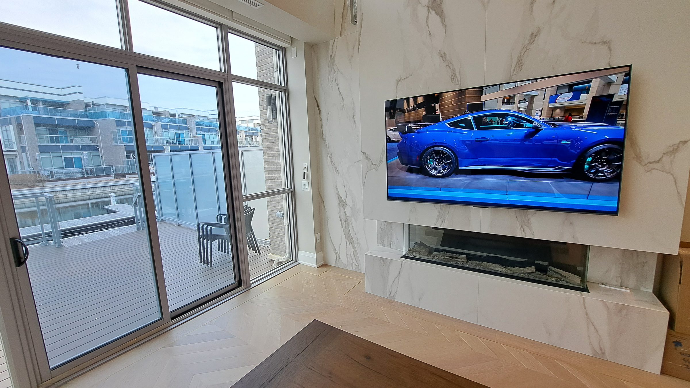 A flush-mounted television above a linear fireplace set into a marble feature wall, beside floor-to-ceiling windows.