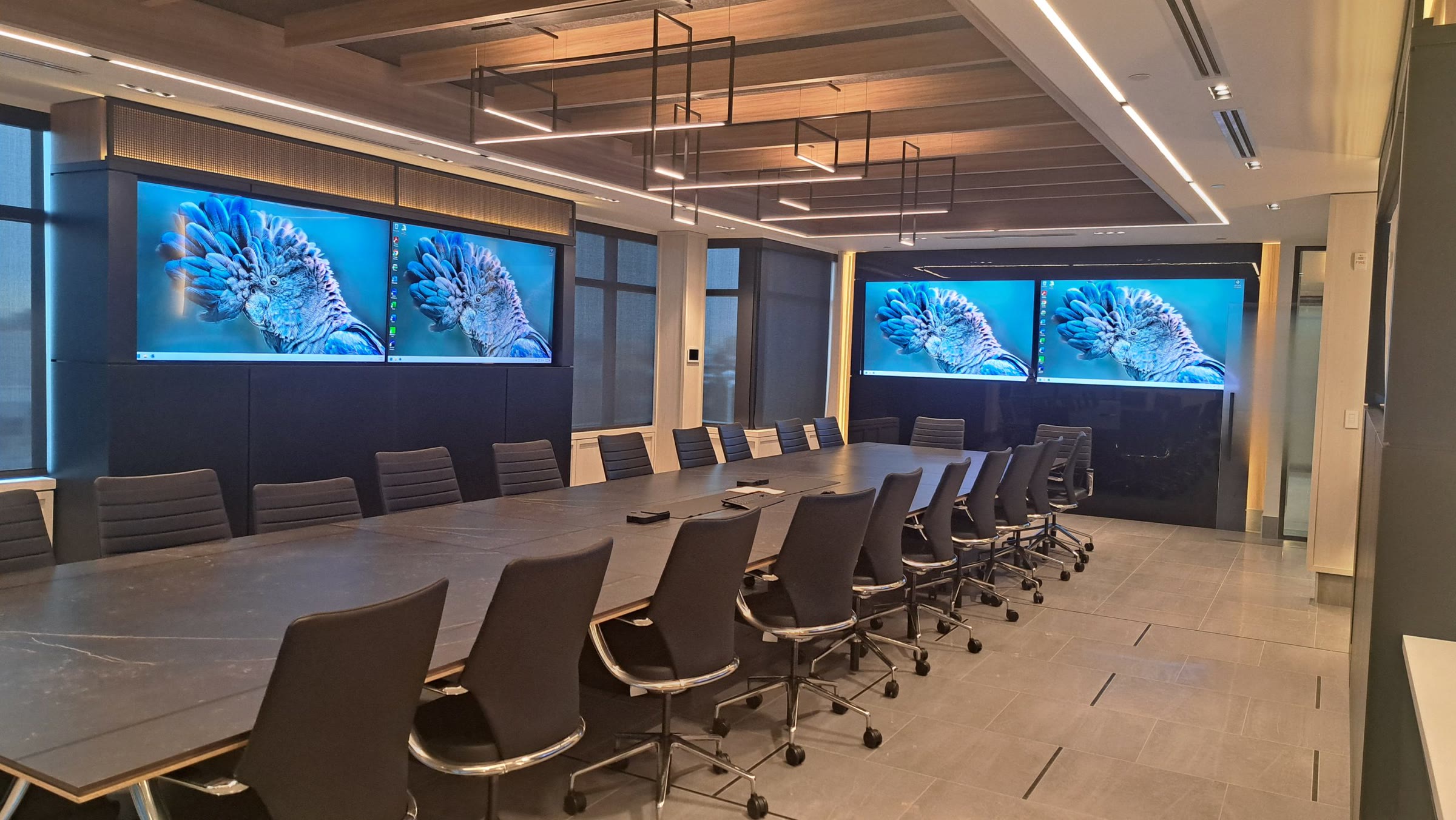 A boardroom with two pairs of large wall-mounted displays flanking a long table.